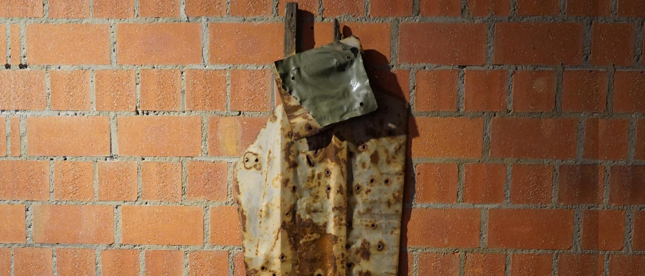 Lädierte Metallplatten, befestigt an zwei senkrechten Holzleisten