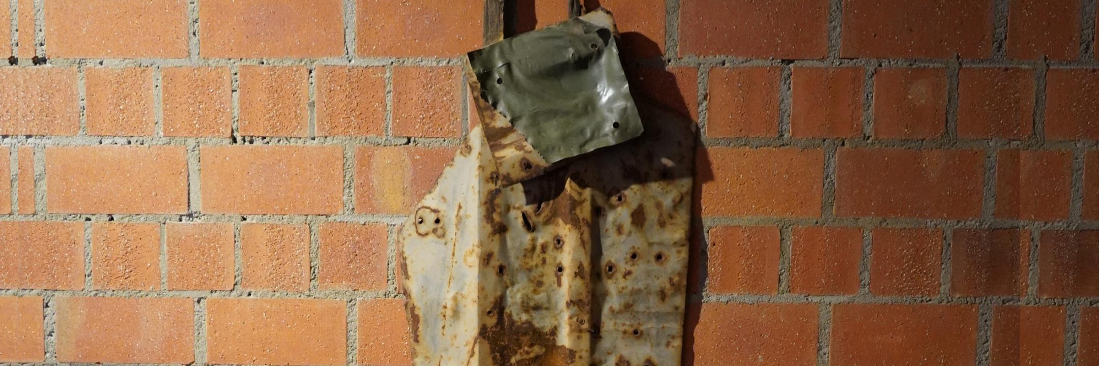 Lädierte Metallplatten, befestigt an zwei senkrechten Holzleisten