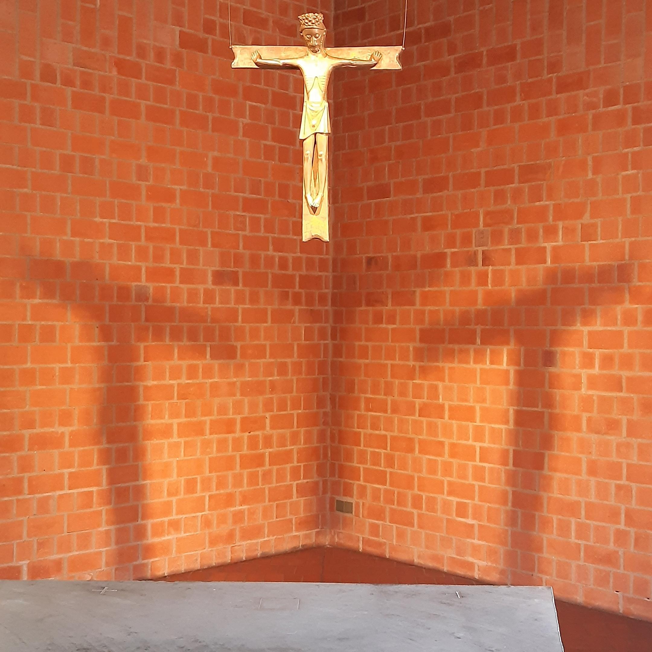 Bronzekreuz mit Christusfigur vor beleuchteter Backsteinwand mit Kreuzschatten