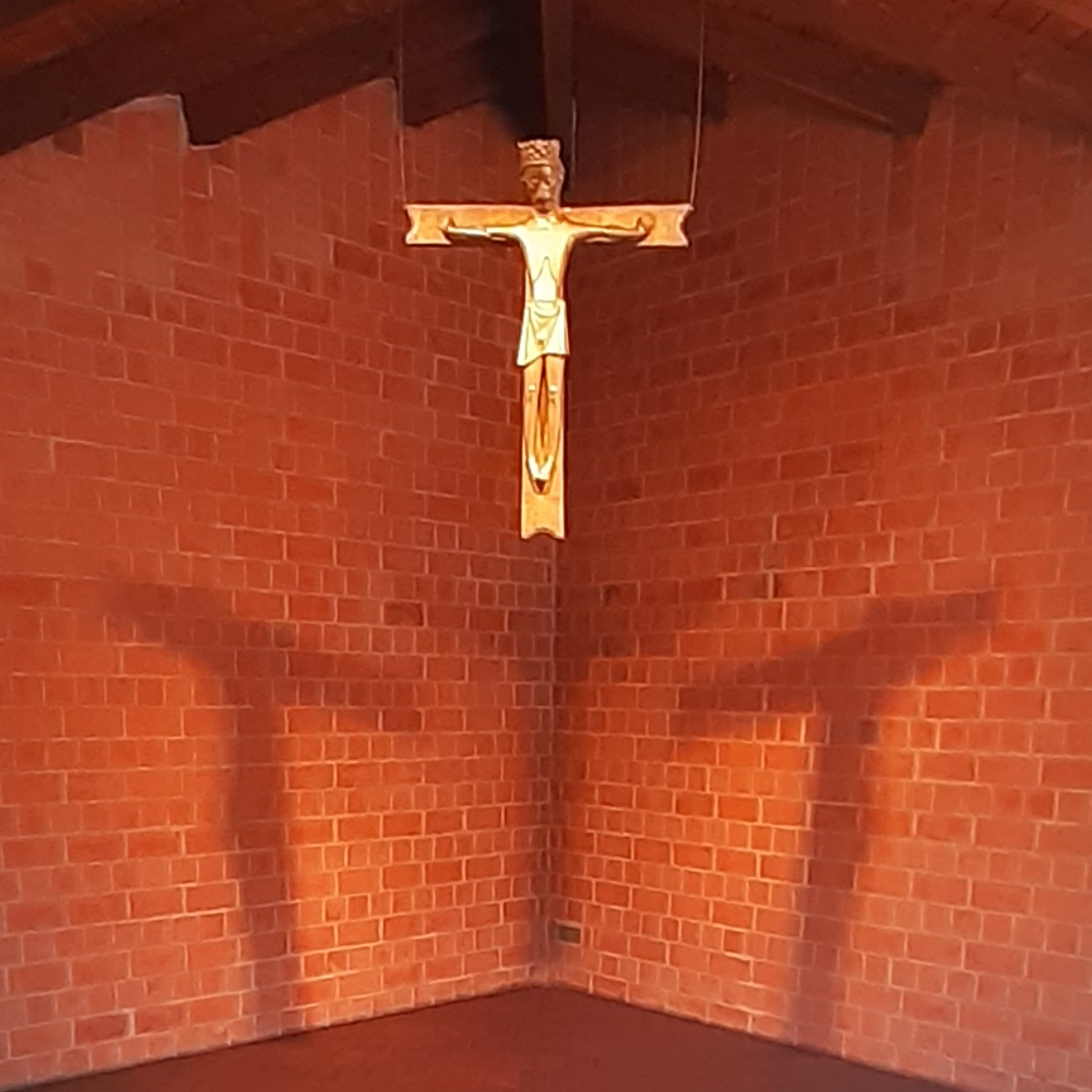 Bronzekreuz mit Christusfigur vor beleuchteter Backsteinwand mit Kreuzschatten