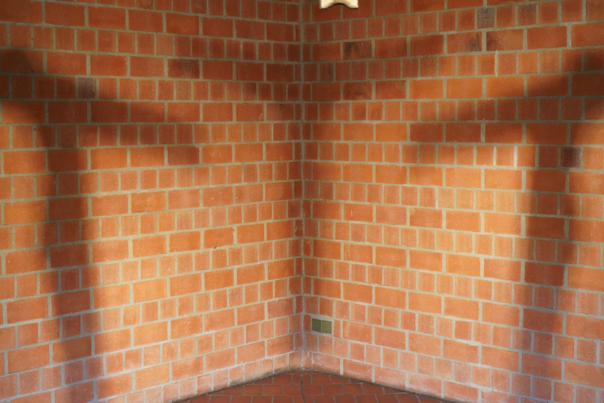 Kreuzschatten der Bronzekreuz mit Christusfigur vor beleuchteter Backsteinwand