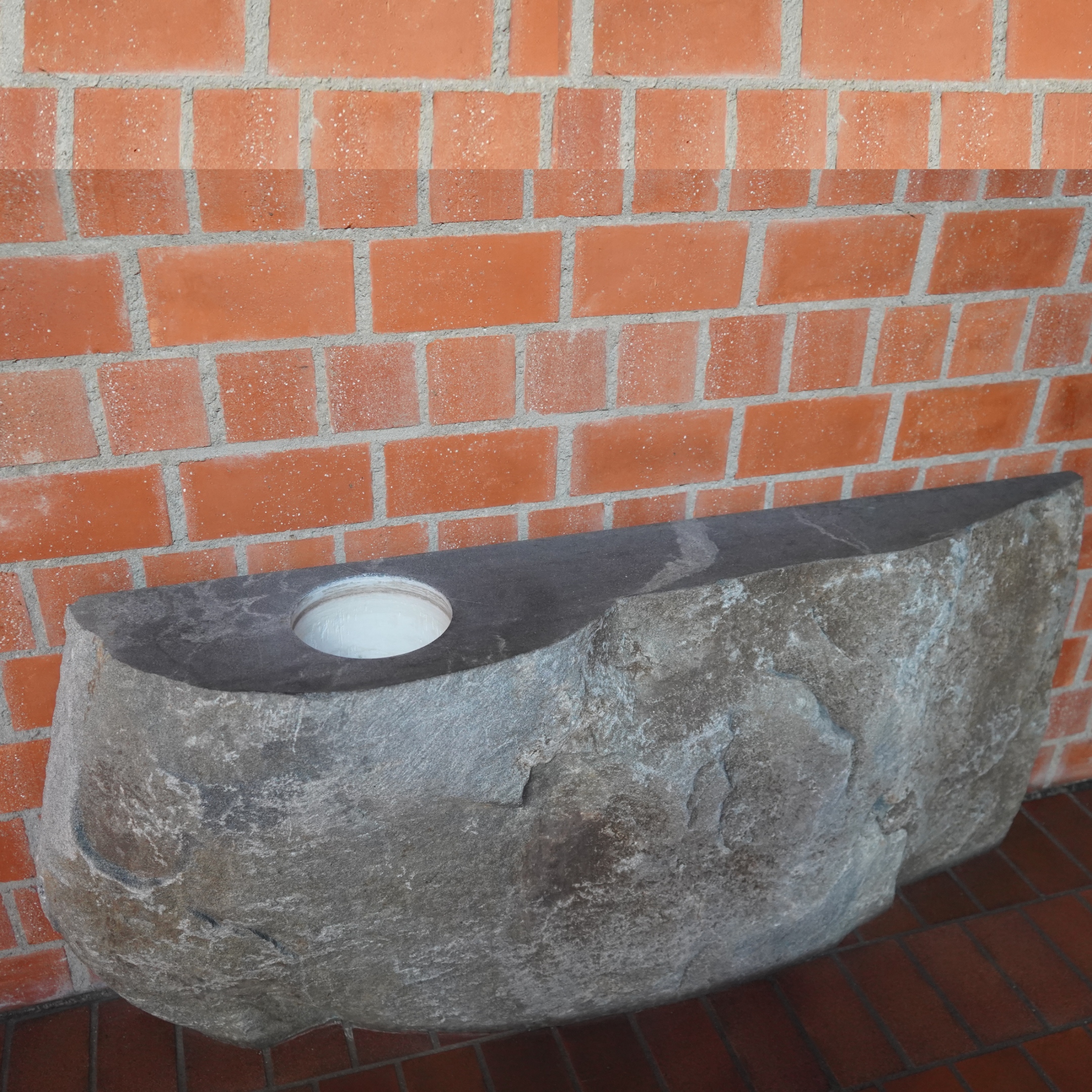 Taufbecken in Granitblock eingearbeitet, vor roter Backsteinwand