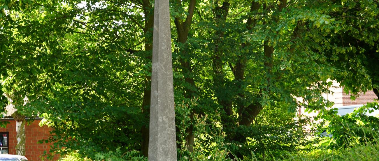 Steinkreuz auf hoher, sich verjüngender Stele im Grünen