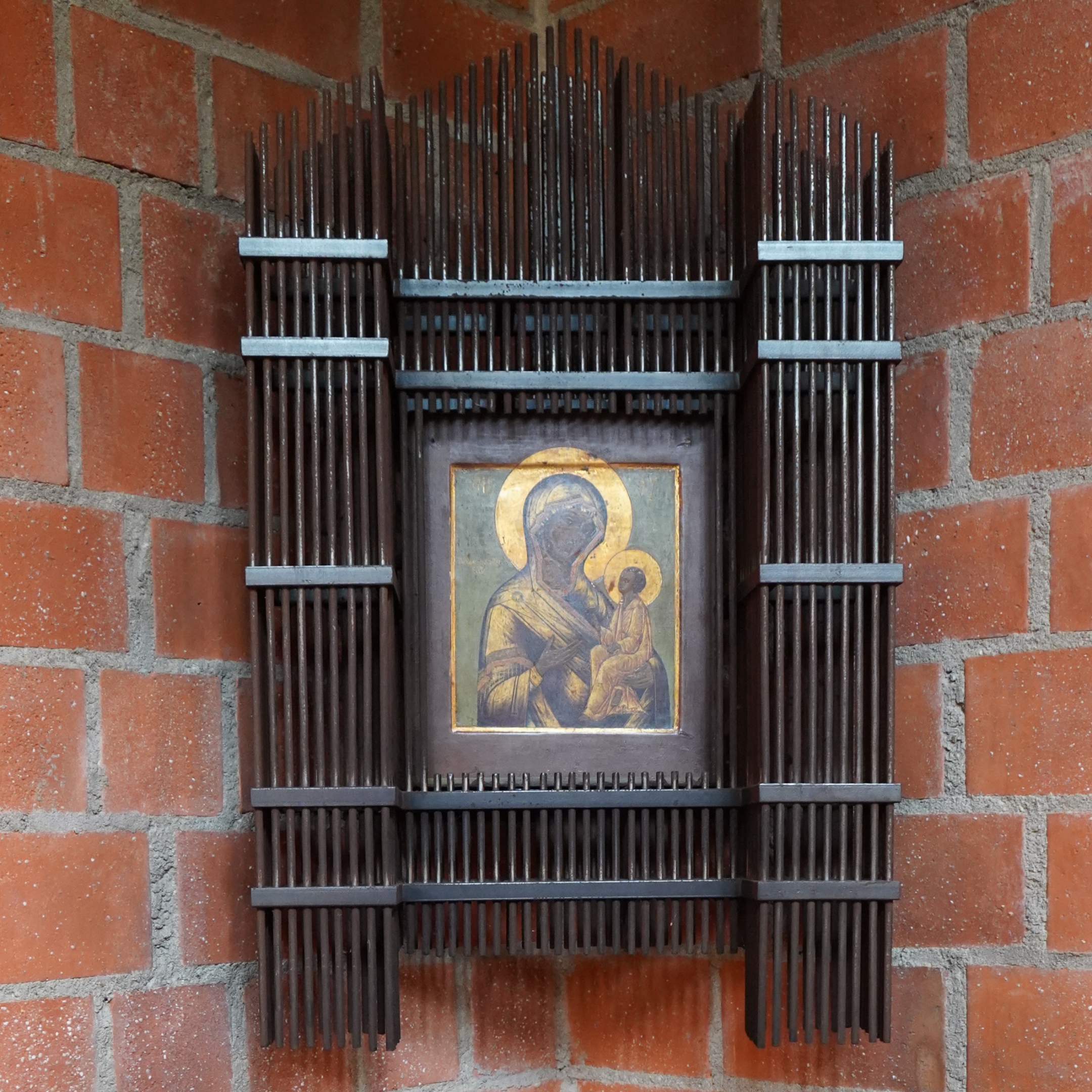 Marienbild mit Kind, umrahmt von senkrechten Stahlstäben mit dachförmigem Abschluss