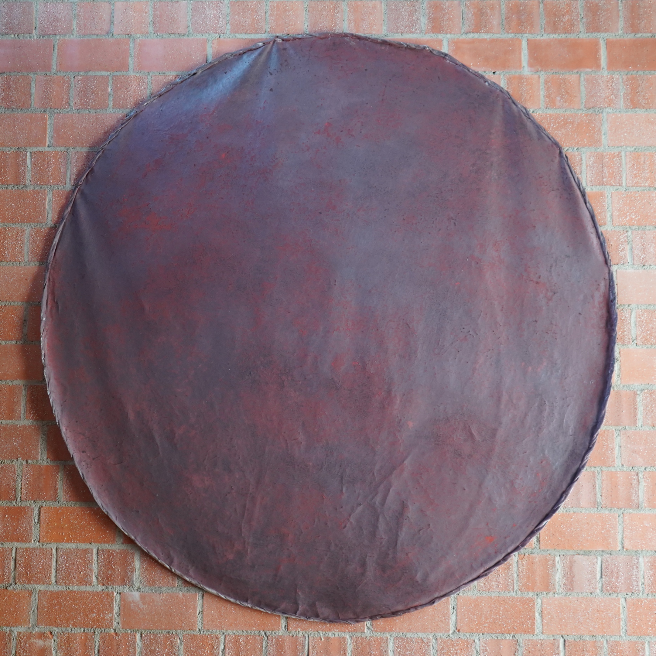 Rotbraun schimmerndes Kreisbild vor roter Backsteinwand