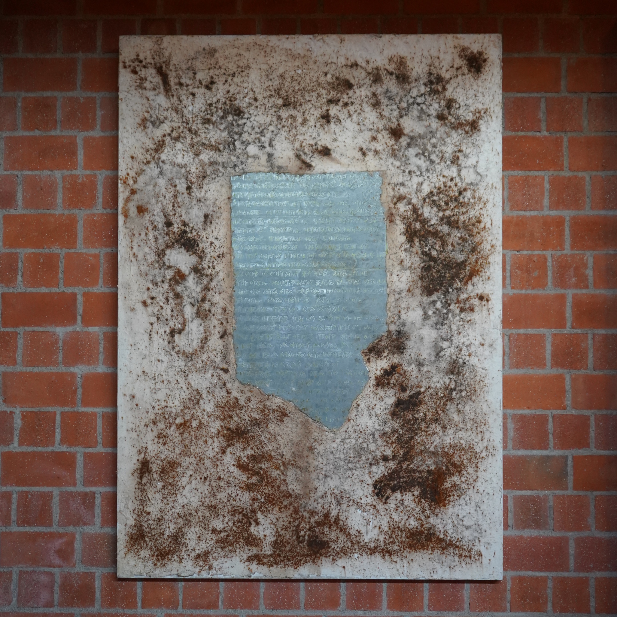 Leinwand mit zentraler Metalltafel und Keilschrift, von Sand umgeben.