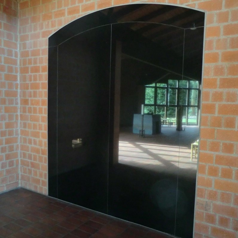 Glänzende Granitplatte in Torform in Backsteinwand eingelassen, spiegelt den Kirchenraum