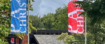 Blick von draußen auf Pax Christi mit roter und blauer Fahne